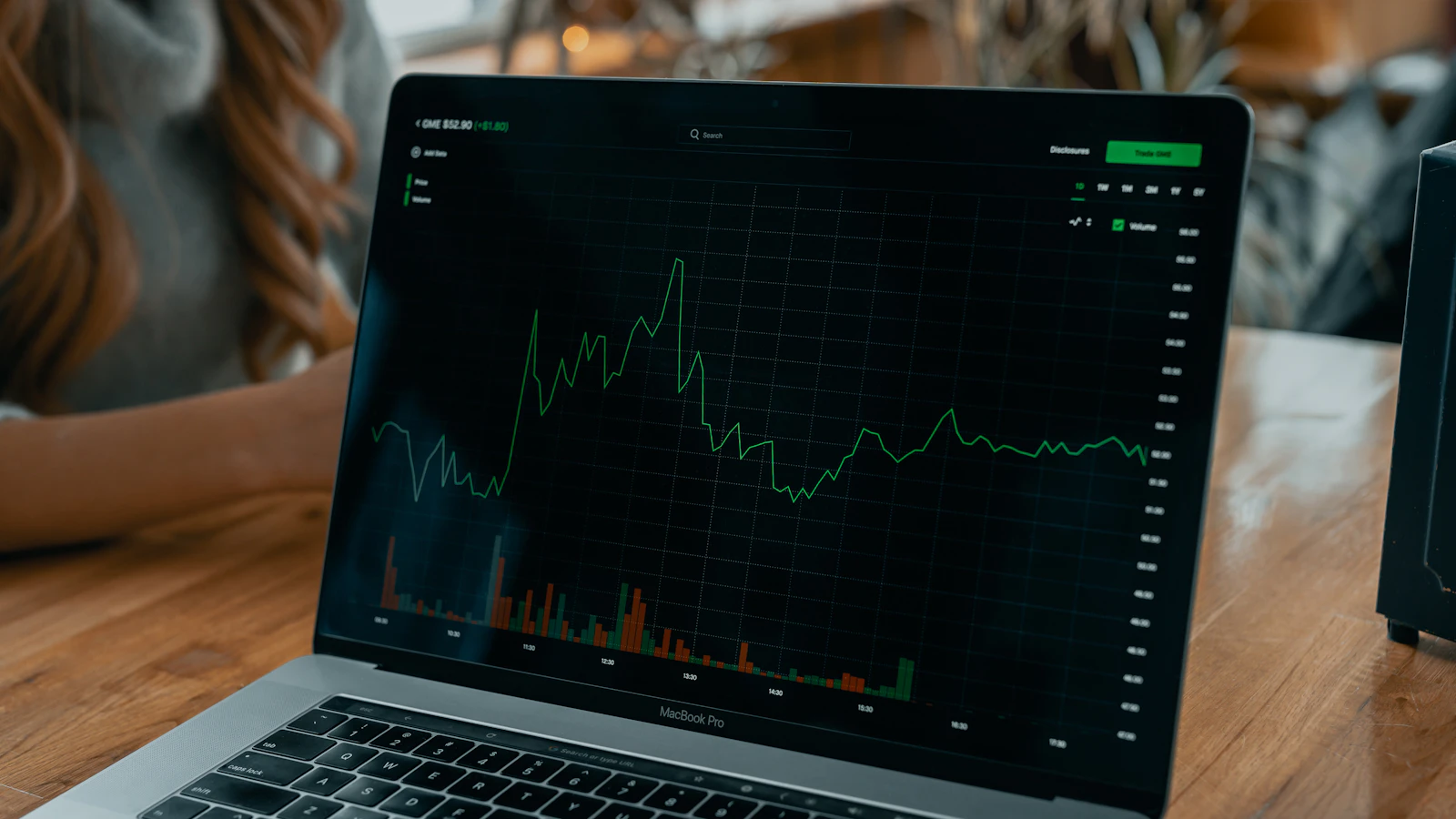 A laptop on a wooden desk displaying a stock price line chart with volume bars