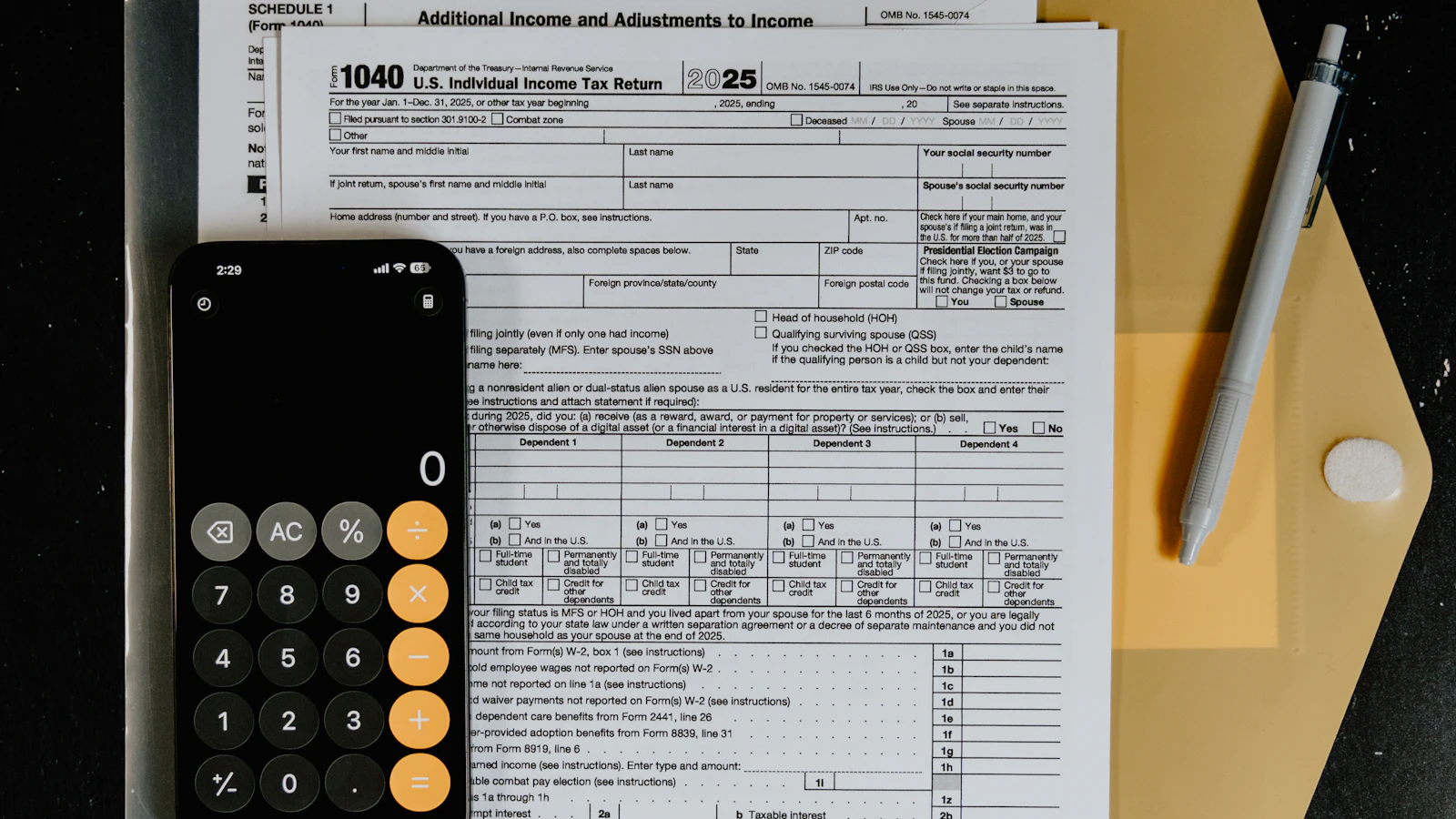 A close-up overhead shot of an IRS 1040 tax form with a calculator and pen resting on top, on a dark desk