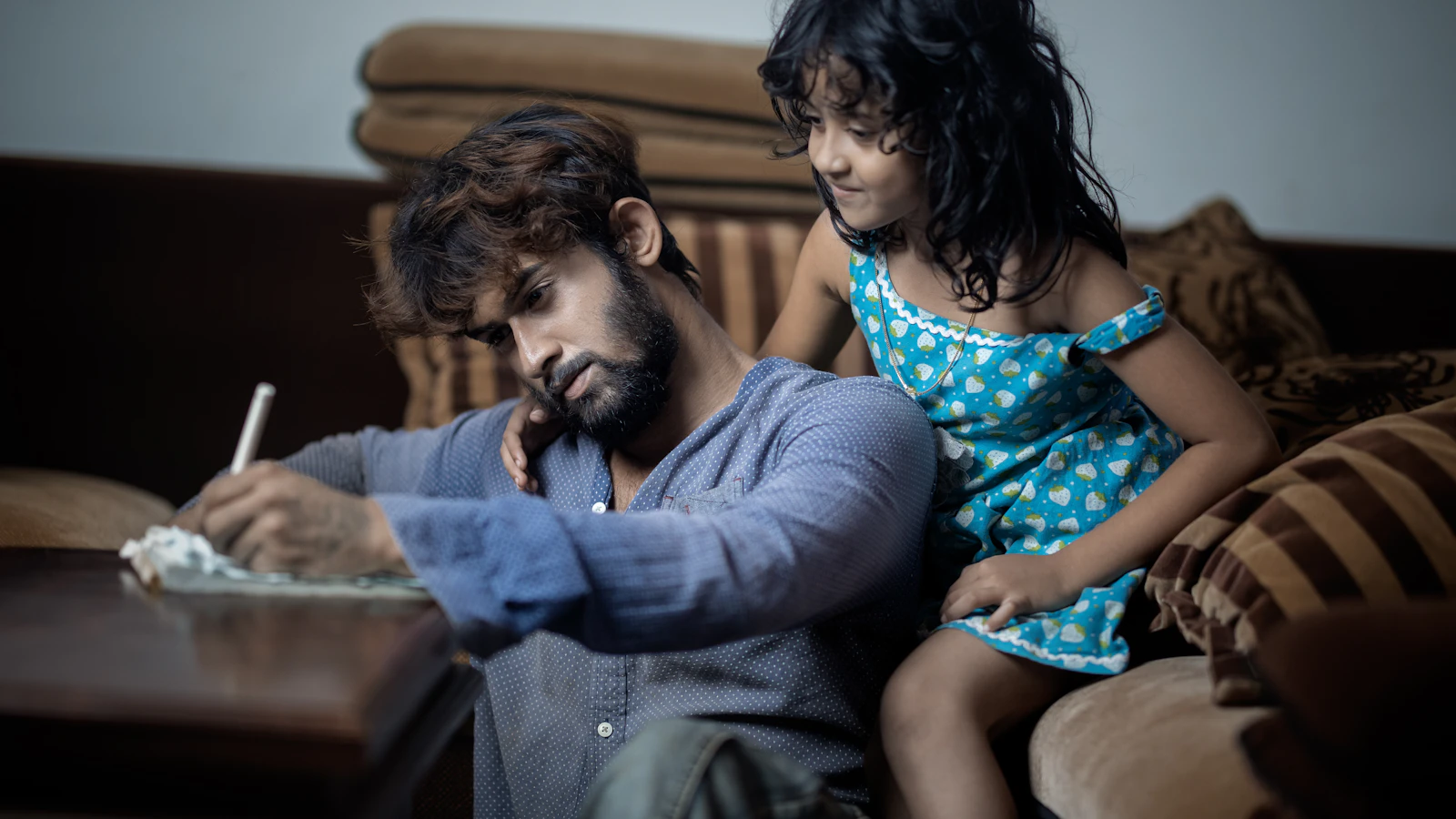 A man writes while a young girl watches him intently