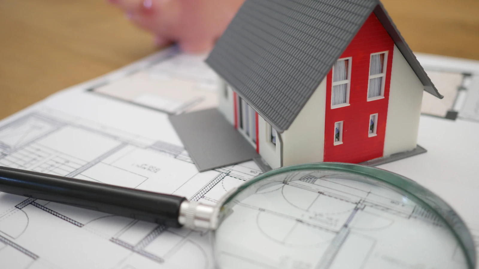 A small wooden model house beside a magnifying glass on a table