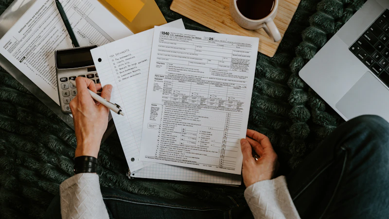 A person reviewing documents with a calculator and laptop