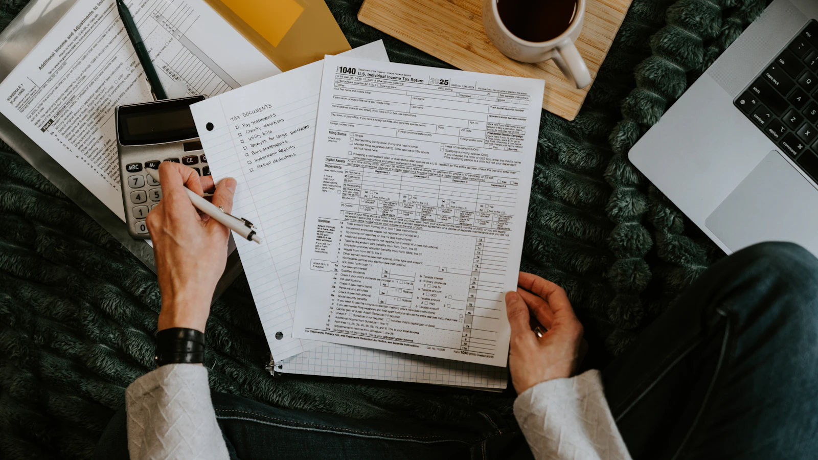 A person reviewing documents with a calculator and laptop