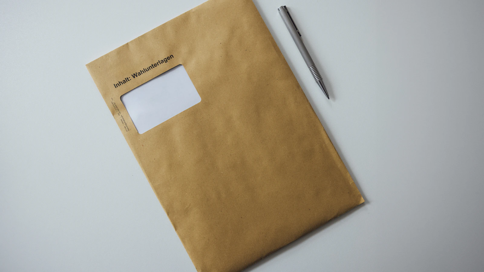 A plain brown window envelope with an official notice inside, lying on a desk next to a pen