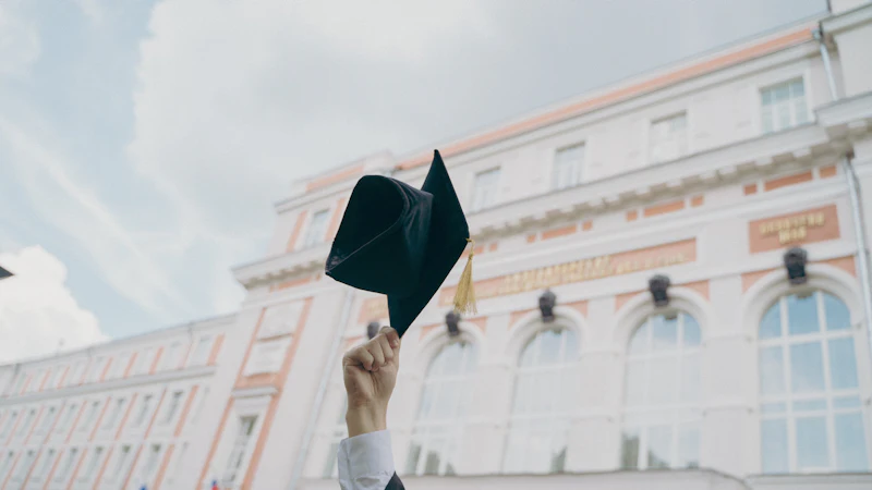 A graduation cap held up in front of a university building