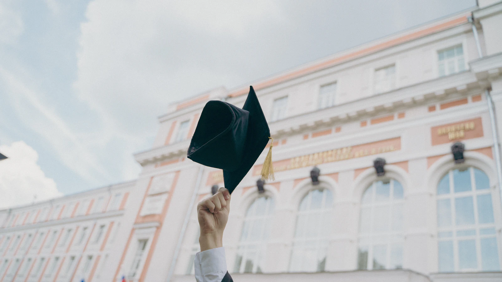 A graduation cap held up in front of a university building