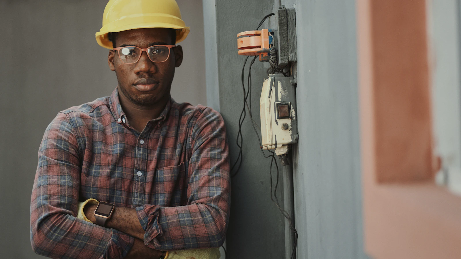 A worker in a hard hat and plaid shirt leaning against a wall